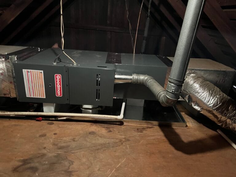 A Goodman HVAC unit is expertly installed in an attic, with ductwork extending from the sides and a beige metal pipe connecting to the right, showcasing professional AC Installation Services.