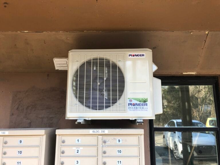AC Repair & Maintenance 9 An air conditioning unit, expertly installed by premier HVAC services, is mounted above the mailboxes on a building wall near a window.
