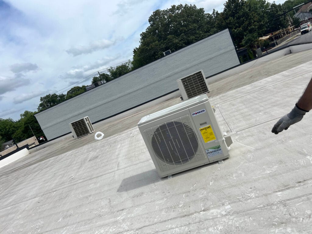 A gloved hand points at air conditioning units on a flat rooftop, creating a dynamic scene under an overcast sky. Trees frame the background, adding depth and context to this unique view, akin to observing dynamic content in a real-world widget.