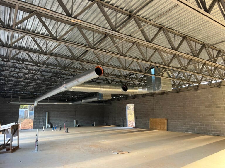 The interior of the construction site features an unfinished ceiling, exposed metal beams, and visible ductwork, creating an industrial atmosphere. Concrete walls and flooring dominate the space, which is perfect for installing a dynamic content widget to bring the area to life.