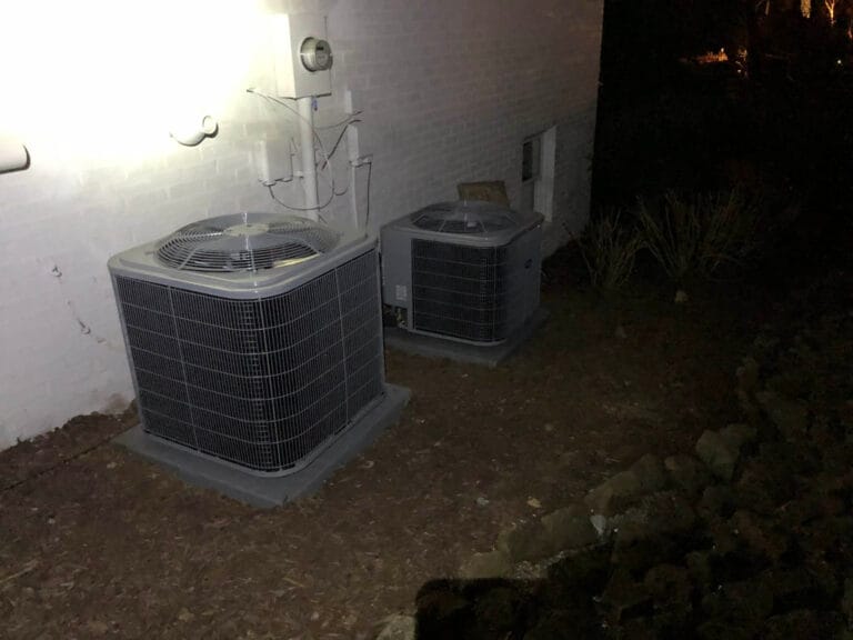 Two outdoor air conditioning units next to a white brick wall, illuminated at night, offering a glimpse of dynamic-content through their quiet hum.