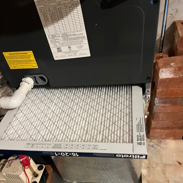 An air filter is installed in an HVAC system by skilled contractors in Georgia, with visible labels and a white pipe connected, set against a backdrop of bricks.