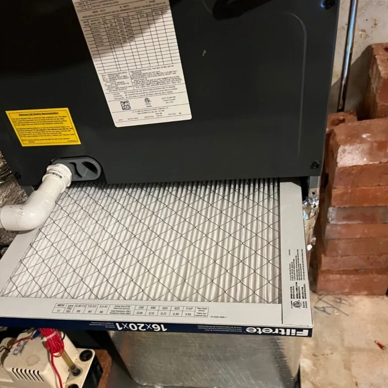 An air filter is installed in an HVAC system by skilled contractors in Georgia, with visible labels and a white pipe connected, set against a backdrop of bricks.