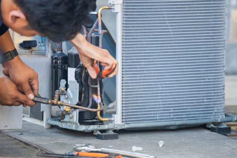 The technician expertly uses a blowtorch on the air conditioning unit's copper piping, holding pliers with precision. Surrounded by various tools, they demonstrate their installation skills in the commercial HVAC field.