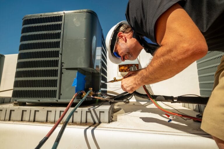 A technician in a helmet and sunglasses expertly handles various tools while working on a rooftop air conditioning unit, showcasing the precision of commercial HVAC installation under a clear sky.