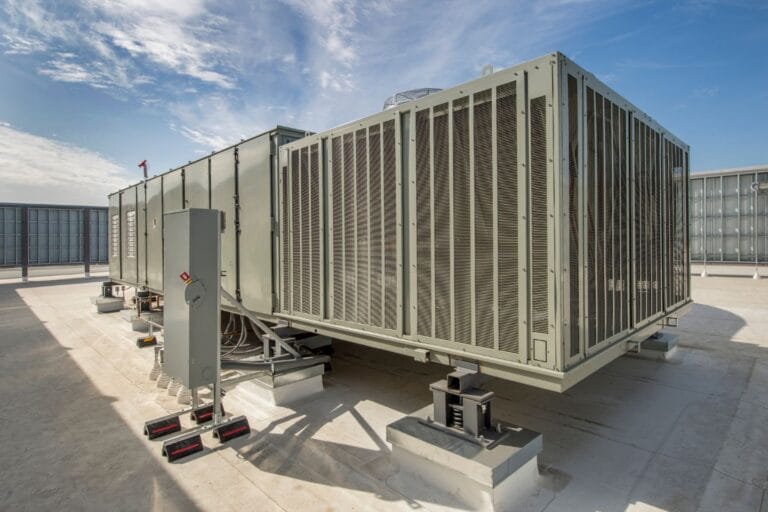 Commercial HVAC installation is evident with the large industrial air conditioning unit perched on a rooftop, encased in a sturdy metal enclosure, all set against the backdrop of a clear blue sky.