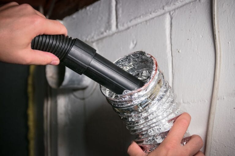 A person expertly performs dryer vent cleaning with a vacuum hose against a sturdy concrete wall.