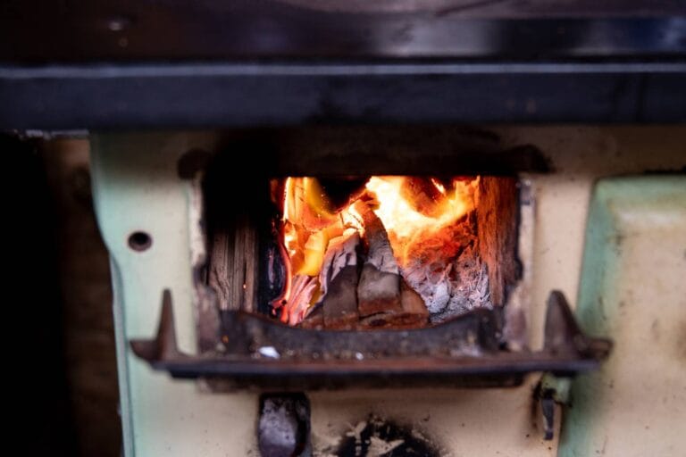 A close-up view of a wood-burning stove with flames visible through the open door, showcasing burning logs and glowing embers—a vivid reminder of the warmth and comfort that proper furnace maintenance brings to your home.