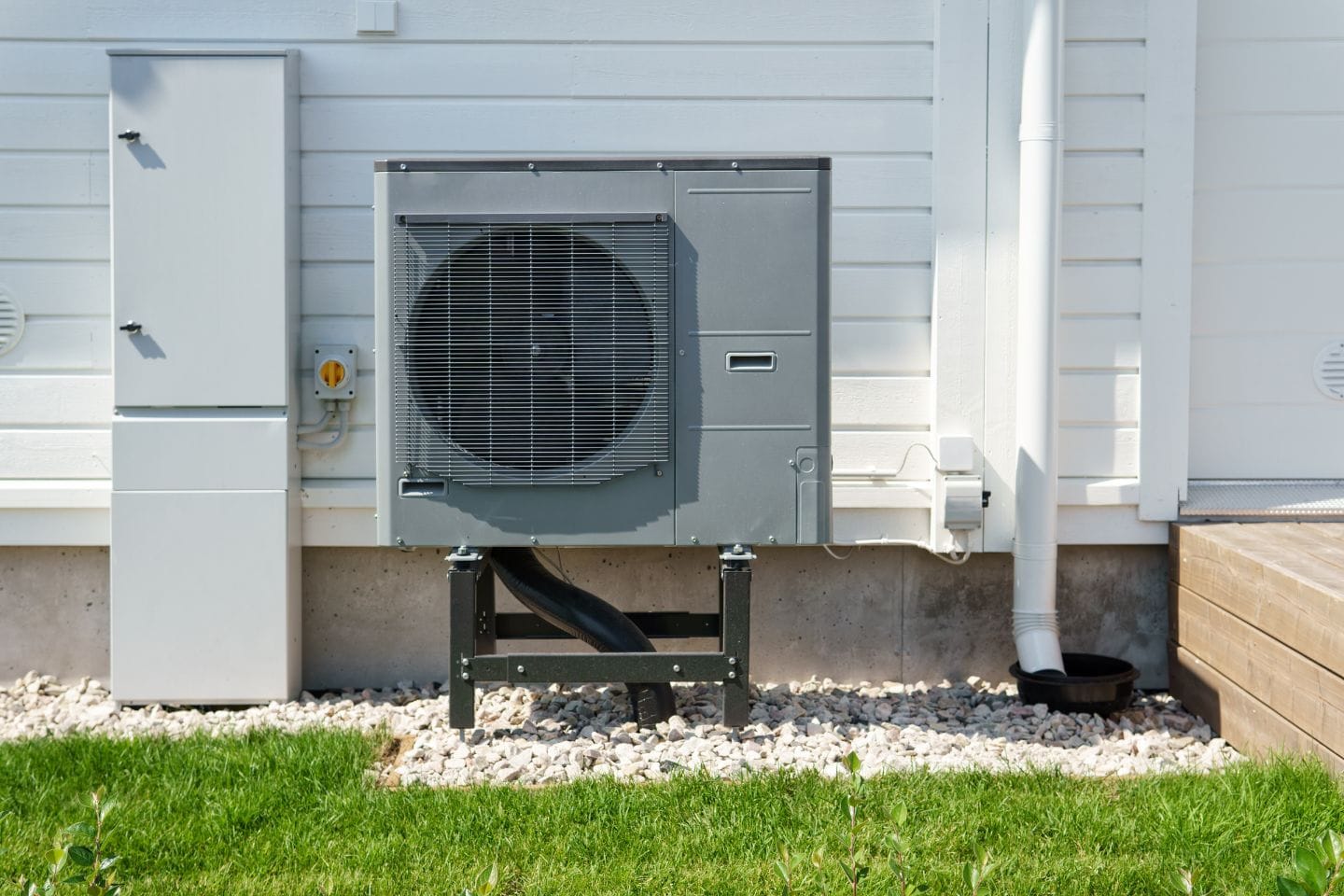 Atlanta Heating Services 6 The outdoor air conditioning unit, resembling a dynamic content widget in design, is mounted on a metal stand near a white building, enhanced by lush greenery and a gravel bed beneath.