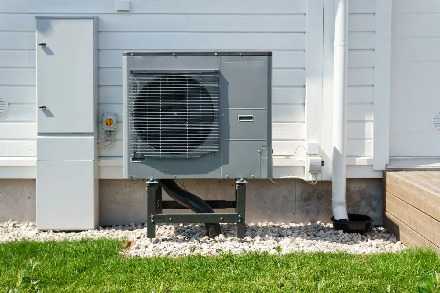 Atlanta Heating Services 6 The outdoor air conditioning unit, resembling a dynamic content widget in design, is mounted on a metal stand near a white building, enhanced by lush greenery and a gravel bed beneath.