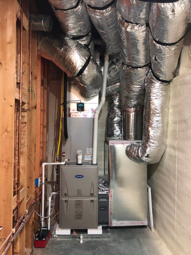 Atlanta Air Quality Services 5 HVAC system with insulated ducts in a utility room. Metal furnace and various pipes are visible. The walls are partially finished with exposed wooden beams, offering a glimpse into professional AC installation and expert HVAC services.