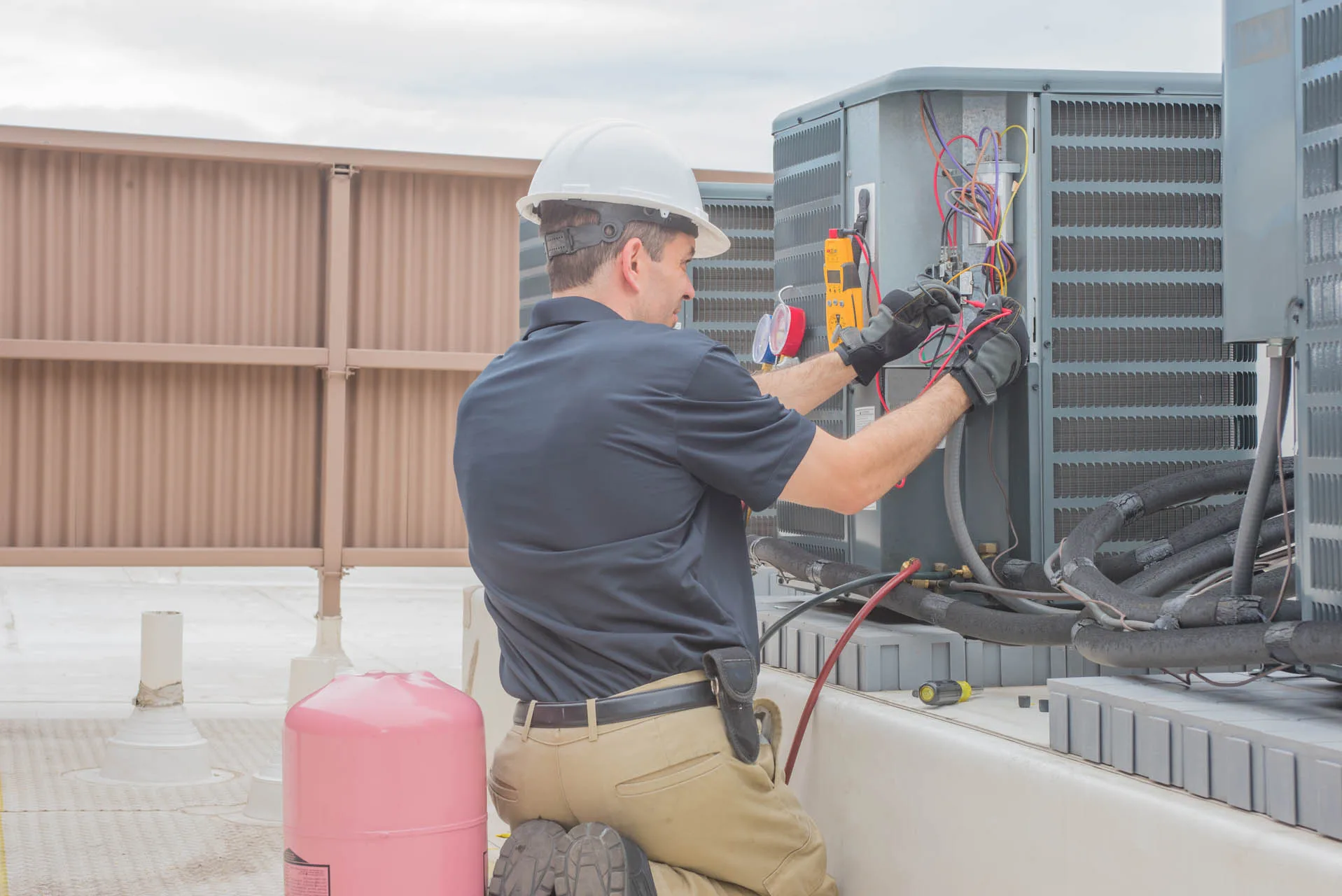 Atlanta Heating Services 3 Technician in a hard hat and gloves repairs a rooftop air conditioning unit with tools and gauges.