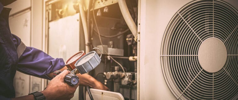 Technician checks air conditioning unit with a pressure gauge, adjusting components, next to a large fan.