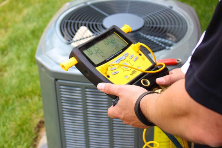 A technician is using a yellow diagnostic tool to check the readings on an outdoor air conditioning unit.