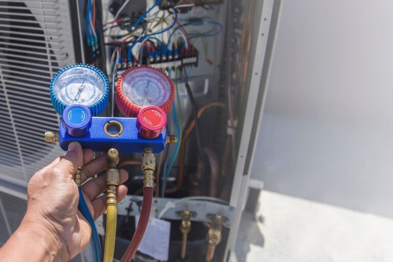 A person conducts HVAC maintenance, carefully holding a pressure gauge while checking the system's tune-ups, revealing various wires and components of the unit.