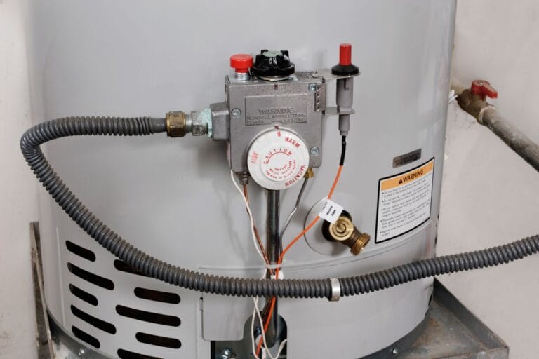 Close-up of a water heater tank with connected pipes and a temperature control valve, featuring warning labels and a metallic exterior. Regular HVAC maintenance, including tune-ups, can help ensure optimal performance and longevity.