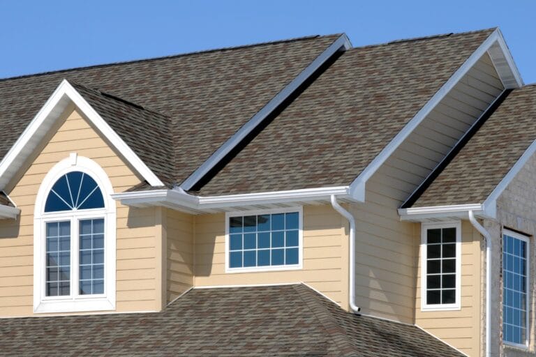 A house with a gable roof, featuring asphalt shingles and an efficient HVAC installation. The exterior boasts yellow siding, three windows, and white trim.