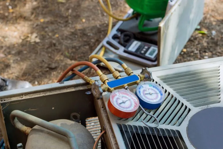 Maintenance plans are in action as an air conditioning unit stands ready, its pressure gauge set attached. Hoses are neatly connected, and a green refrigerant cylinder is poised in the background on a dirt surface, ensuring seamless care for residential comfort.