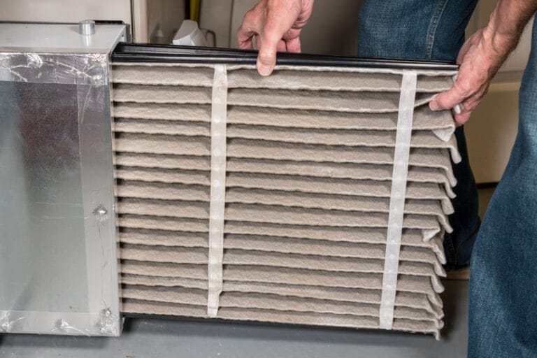A person expertly removes a dirty air filter from an HVAC unit, showcasing the importance of residential maintenance in ensuring efficient home upkeep.