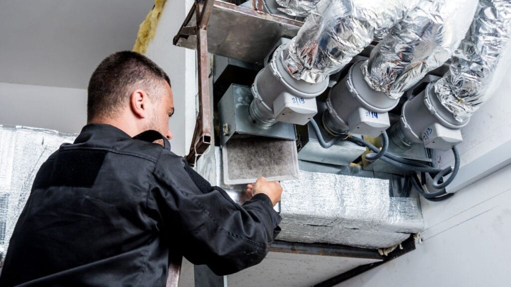 A technician in a black uniform is meticulously performing commercial HVAC maintenance in Georgia, handling components and inspecting ductwork in an industrial setting somewhere in Georgia.