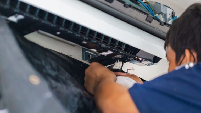A technician in a blue shirt, focusing intently, is expertly repairing an air conditioning unit. His skilled hands adjust the components with precision, ready to tackle any emergency AC repair in Georgia.