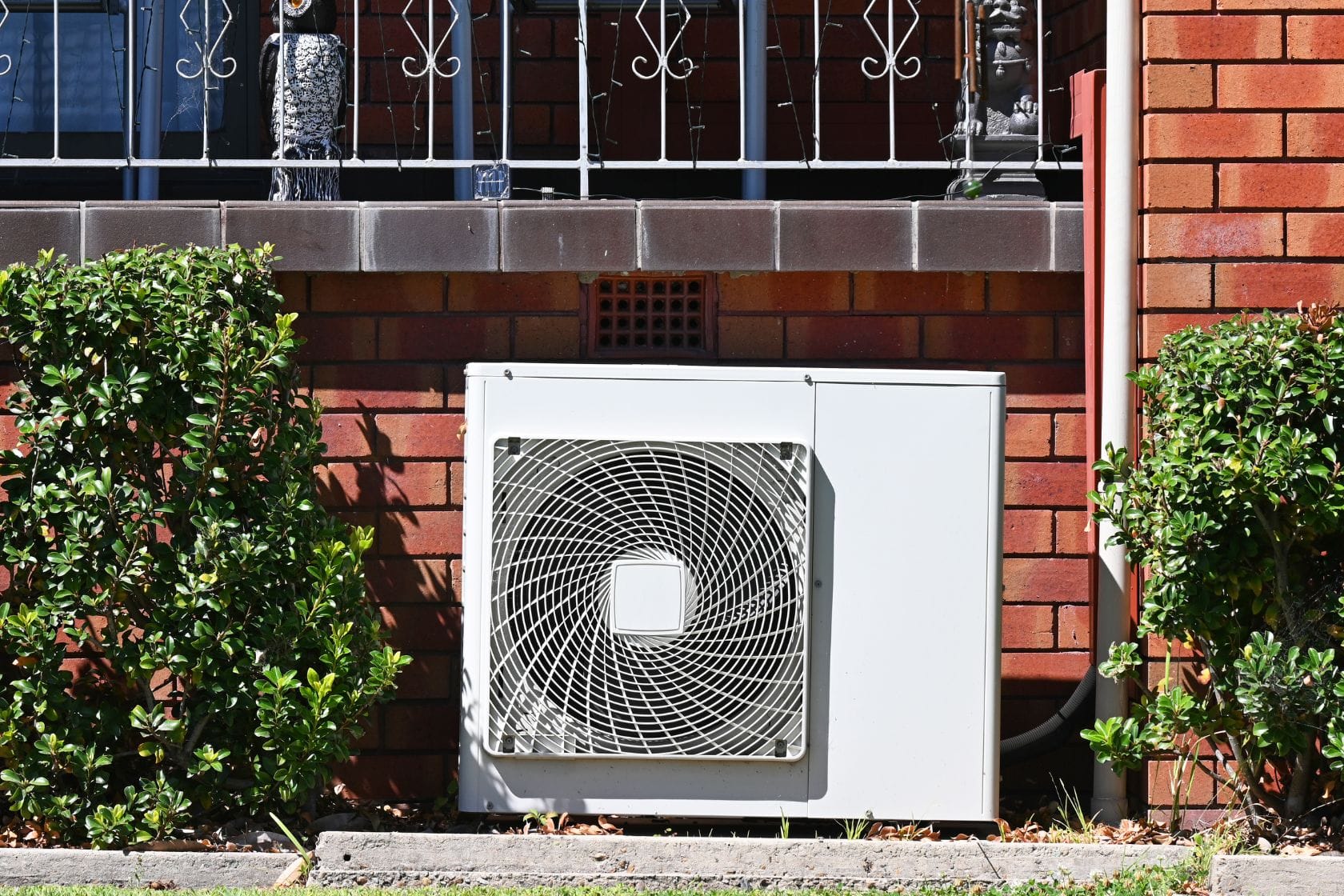 Atlanta Air Quality Services 3 An outdoor air conditioning unit, expertly installed between two lush shrubs on a brick wall, ensures efficient climate control. Discover top-notch services that guarantee your comfort and satisfaction.