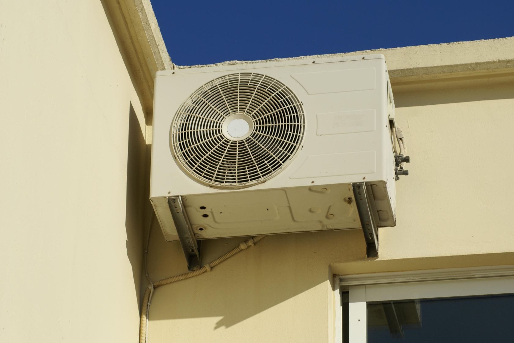 AC Repair & Maintenance 6 A wall-mounted HVAC unit clings to the cream-colored building, effortlessly blending with the serene blue sky backdrop.