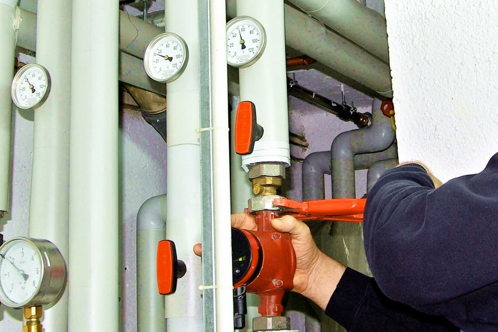 Atlanta Heating Services 1 Heating Services in Atlanta: In a maze of pipes and gauges, a person carefully adjusts a red valve with a wrench, showcasing the intricacies of an HVAC system.