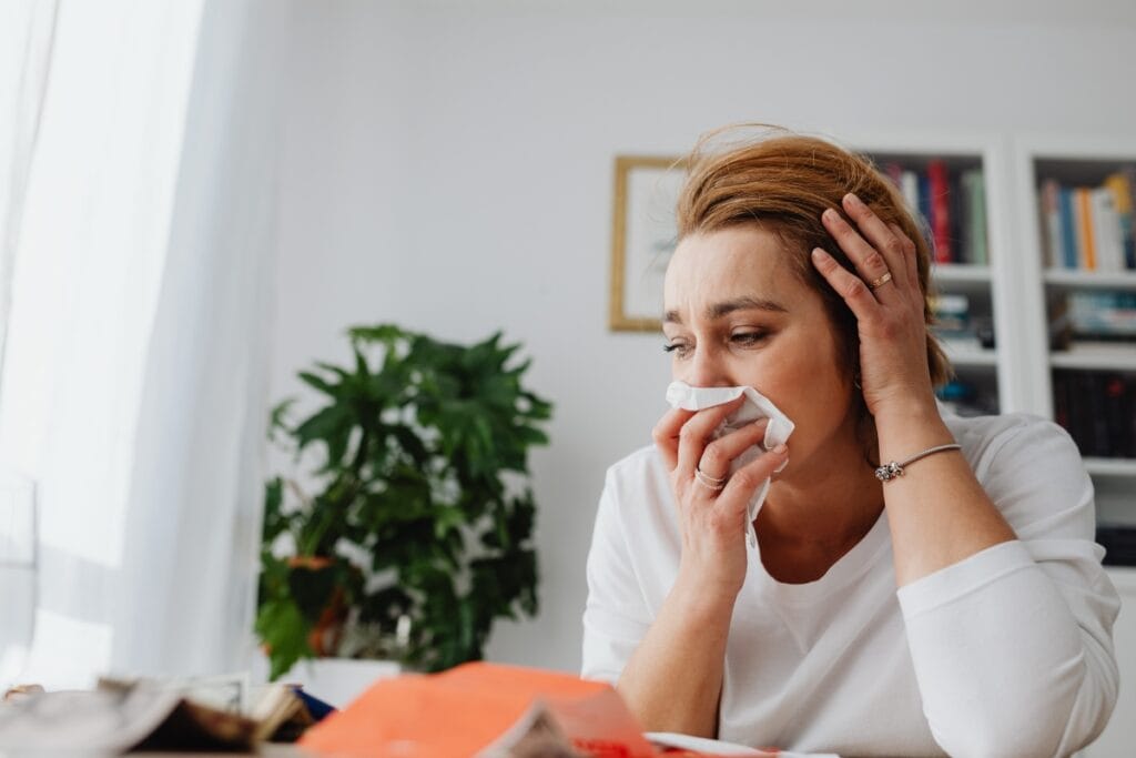 Best Air Purifiers for Allergies: Improve HVAC Air Quality 2 Woman sitting indoors holds a tissue to her nose with one hand and rests her head on the other, appearing unwell or upset—highlighting the need for air purifiers for allergies.