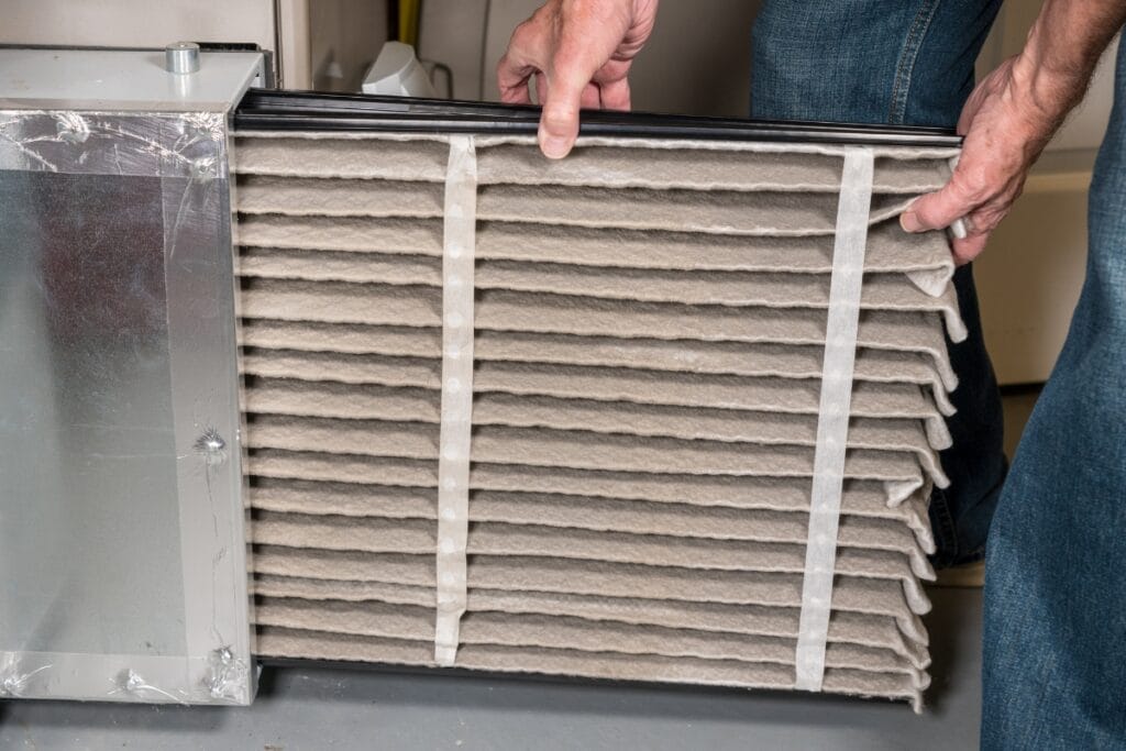 HVAC Maintenance Tips Every Pet Owner Should Know 4 A person is performing HVAC maintenance by removing a dirty air filter from a residential system.