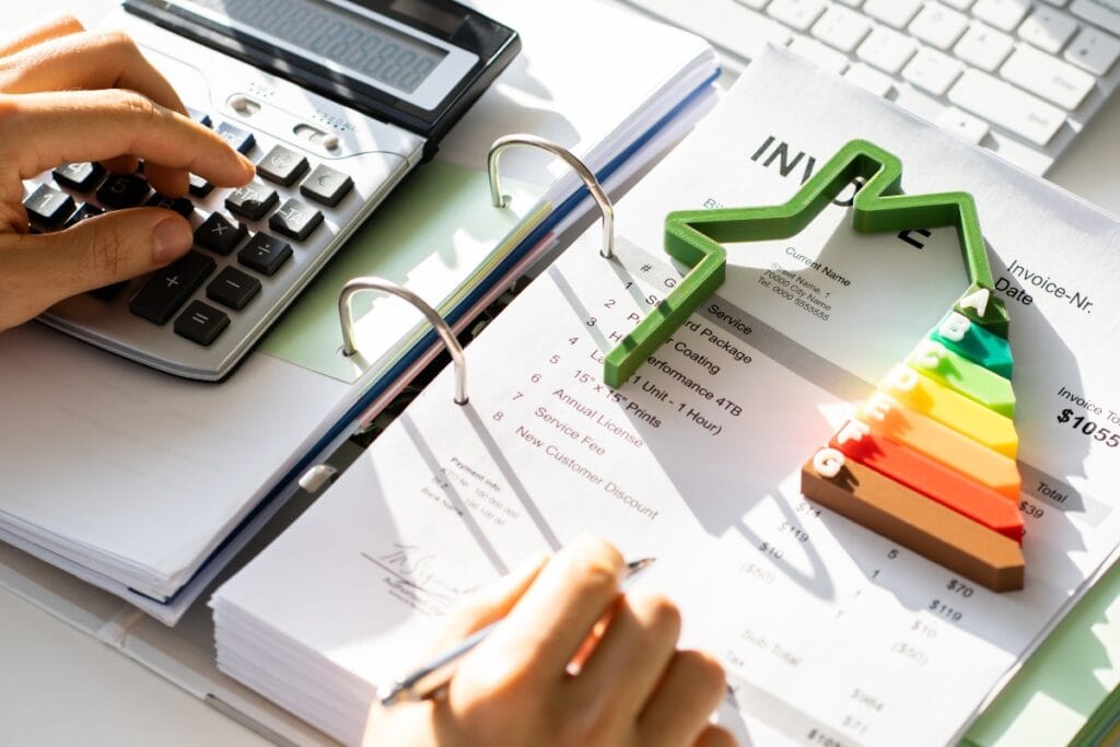 The Ultimate SEER Rating HVAC Guide: Why It’s Crucial for Efficiency 4 Person using calculator and reviewing invoices with a rising arrow and energy efficiency chart, referencing SEER rating HVAC systems, on top of paperwork next to a computer keyboard.