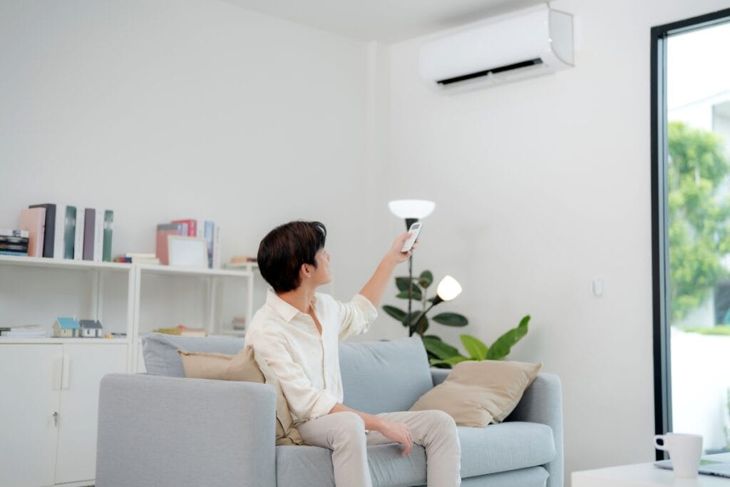 Ductless HVAC Systems: Pros and Cons of Mini-Splits 9 A person sitting on a sofa in a modern living room uses a remote control to operate a wall-mounted ductless HVAC air conditioner.