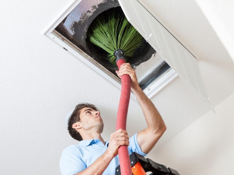 Atlanta Air Quality Services 10 A person uses a large brush and vacuum to clean an air duct through an open ceiling vent, ensuring improved indoor air quality services in Georgia.