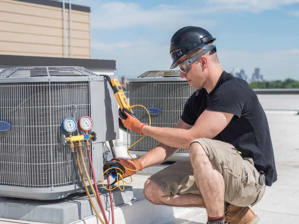 Commercial HVAC Maintenance Tips for Fall 10 A technician wearing safety gear uses diagnostic tools to inspect rooftop commercial HVAC units on a sunny day, following essential fall HVAC tips for proper commercial HVAC maintenance.