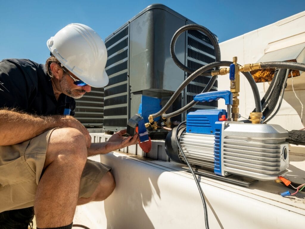 Commercial HVAC Maintenance Tips for Fall 15 A technician wearing a hard hat inspects an HVAC unit on a rooftop, using gauges and tools connected to the equipment as part of routine commercial HVAC maintenance.