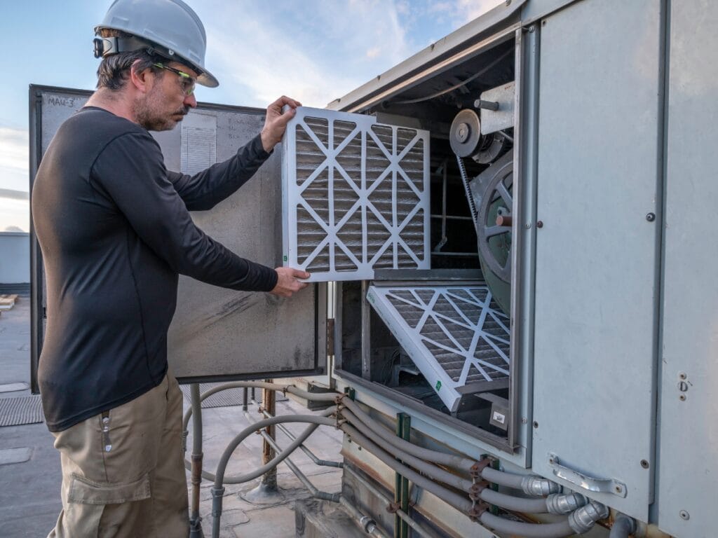 Commercial HVAC Maintenance Tips for Fall 16 A worker wearing safety gear replaces air filters in a commercial HVAC unit on a rooftop, following key fall HVAC tips for proper commercial HVAC maintenance.
