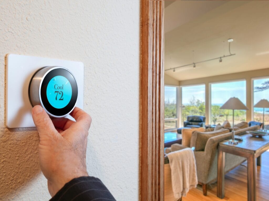 Commercial HVAC Maintenance Tips for Fall 12 A hand adjusts a smart thermostat set to 72 degrees on a wall, with a modern living room and large windows in the background—perfect inspiration for seasonal HVAC tips or reminders about fall maintenance.