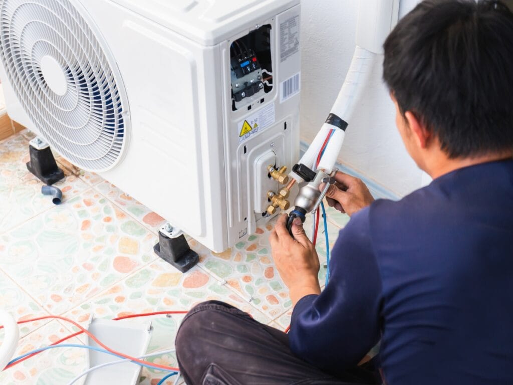 A technician uses an HVAC Checklist while installing or repairing an outdoor air conditioning unit, carefully connecting pipes and wiring on a tiled floor.