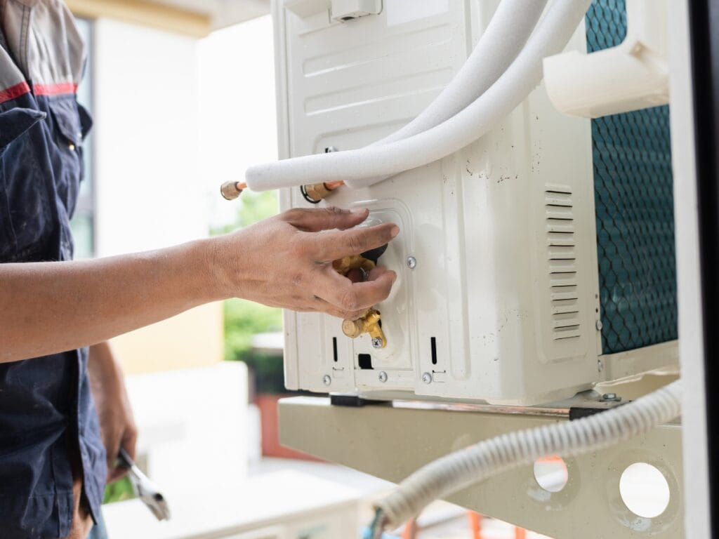 A person adjusts valves on the back of an outdoor air conditioning unit during installation or maintenance, helping prevent issues like mold in HVAC systems.