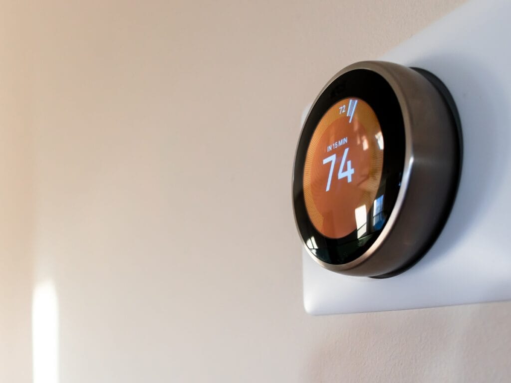 A programmable thermostat mounted on a beige wall displays an indoor temperature of 74 degrees Fahrenheit.