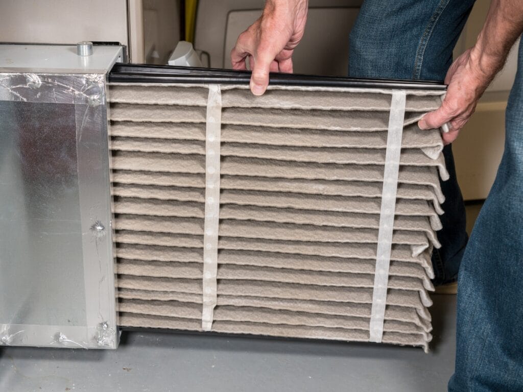 A person removes a dirty air filter from an HVAC system, showing accumulated dust and debris—a key task on the furnace maintenance checklist.