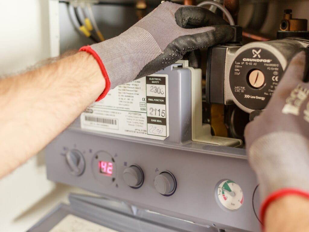 A person wearing gloves adjusts components inside a boiler system, with a digital display showing 42 and control dials visible—demonstrating essential end of year HVAC tips for optimal performance.