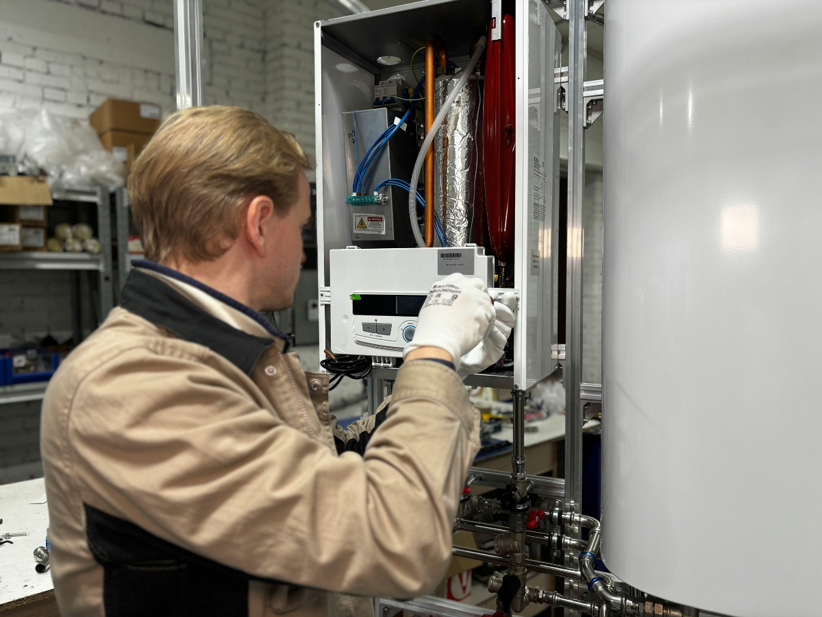 A technician wearing gloves examines and adjusts Beginners Components wiring inside the open control panel of industrial equipment in a workshop setting.
