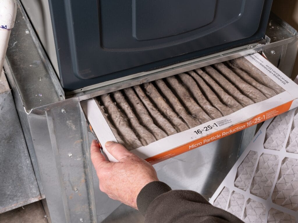 Troubleshooting Furnace Not Heating for Metro Atlanta Homeowners 3 A person troubleshooting furnace not heating issues by removing a dirty air filter from a home HVAC system for replacement.