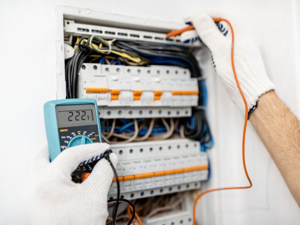 Troubleshooting Furnace Not Heating for Metro Atlanta Homeowners 4 Person wearing gloves uses a digital multimeter to measure voltage in an open electrical panel, troubleshooting furnace not heating amid various wires and circuit breakers.