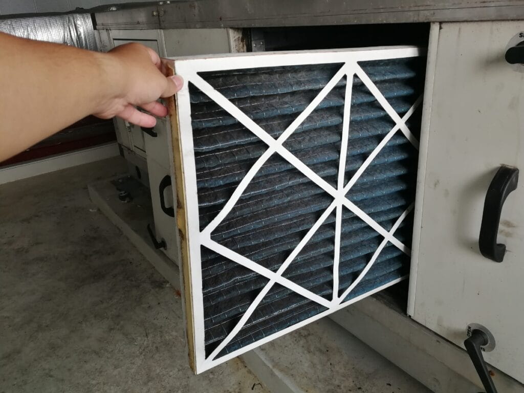 A person is removing a dirty air filter from an HVAC unit in an indoor setting, following tips from an air filter guide.