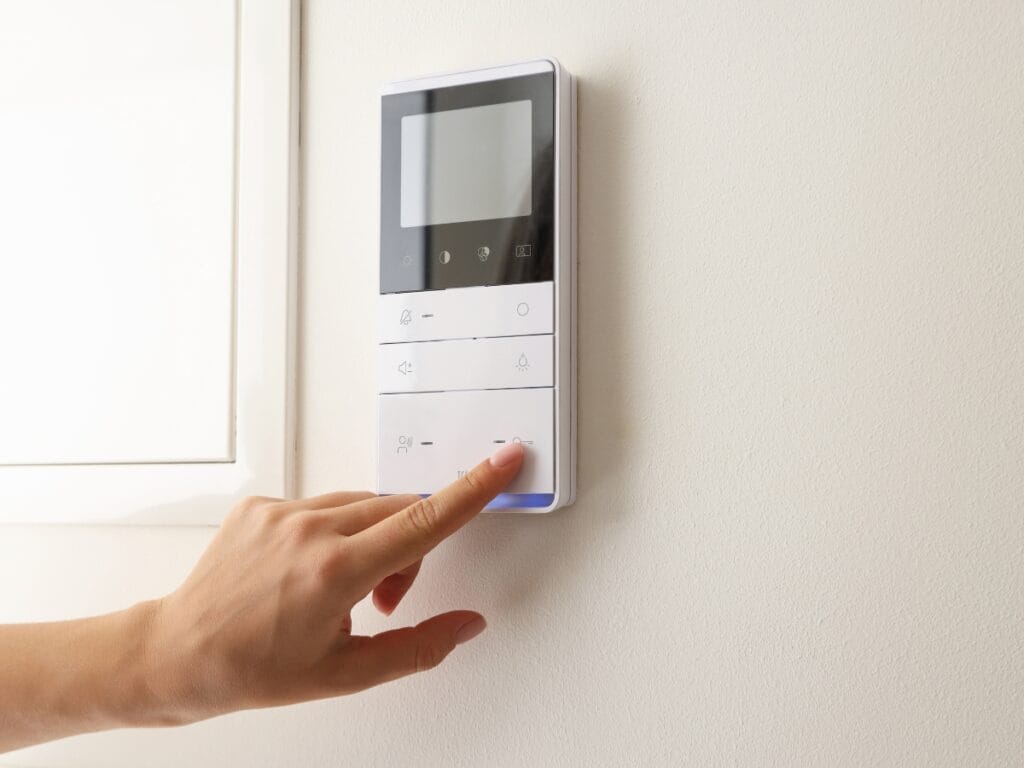 Seasonal Vacation Prep: How to Save Energy Efficiently While Away 1 A hand presses a button on a modern wall-mounted control panel with a screen and several touch buttons—perfect for seamless Seasonal Vacation Prep.