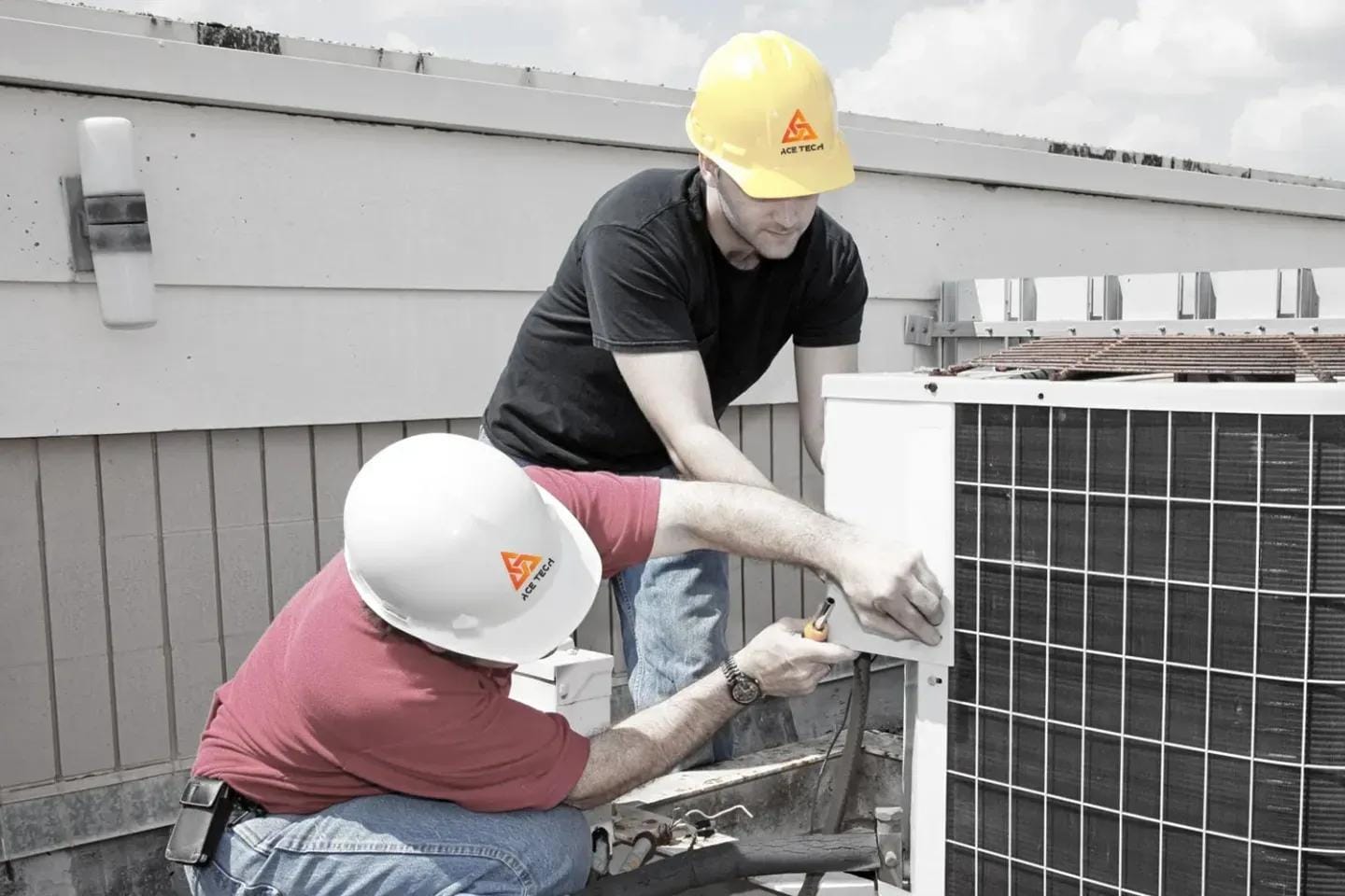 Two technicians in hard hats working on an outdoor air conditioning unit.