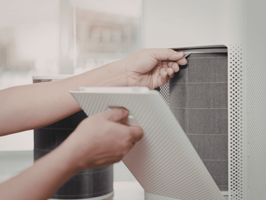 A person is removing a protective cover and filter from a white air purifier for maintenance or replacement, helping to improve health by reducing pet dander in the home.