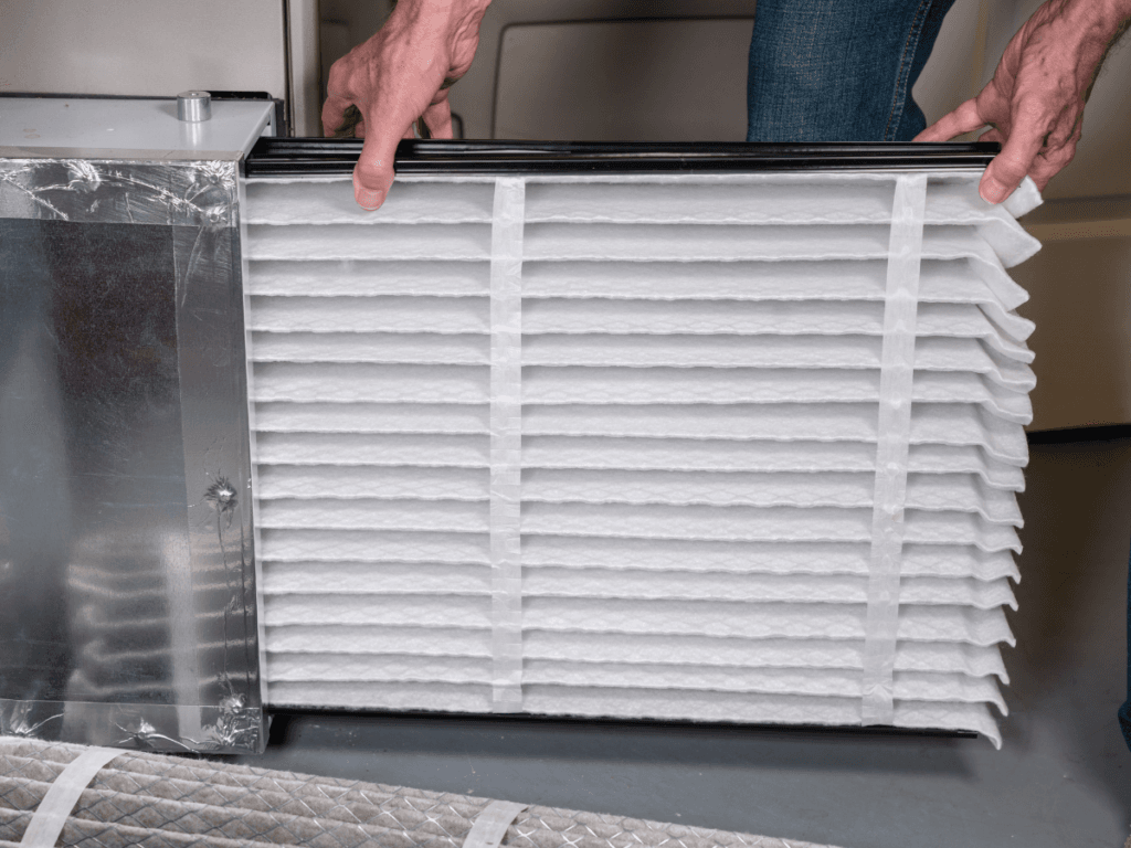 A person installs a clean pleated air filter into a metal HVAC unit, promoting health by reducing pet dander, with hands visible holding the filter in place.